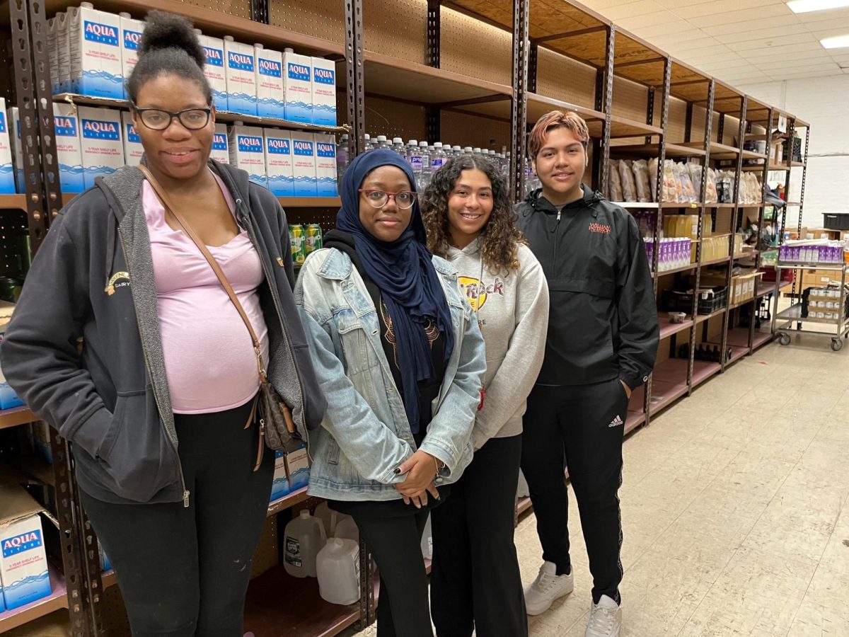 Students Camryn Rayfield, Sabriyah Satterfield-Ali, Solenni Gonzalez, and Jason Peralta stand in front of a shelf of beverages at the food pantry in Father English Community Center.  Photo courtesy of William Paterson University Honors College